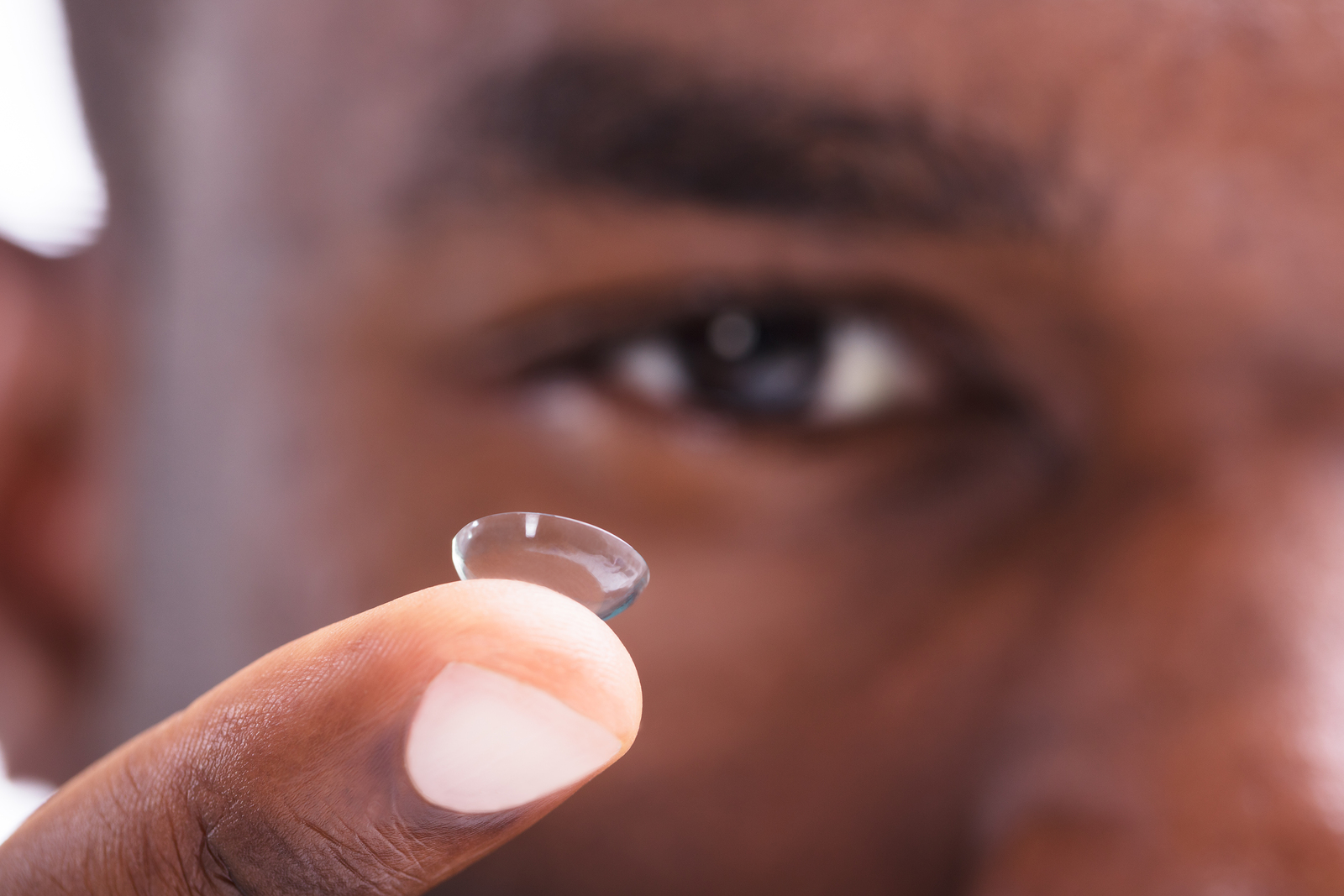 man holding a contact lens on his finger
